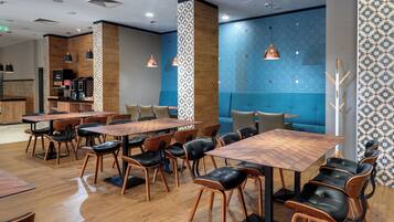 A modern restaurant with wooden tables and chairs, a blue accent wall, and pendant lighting.