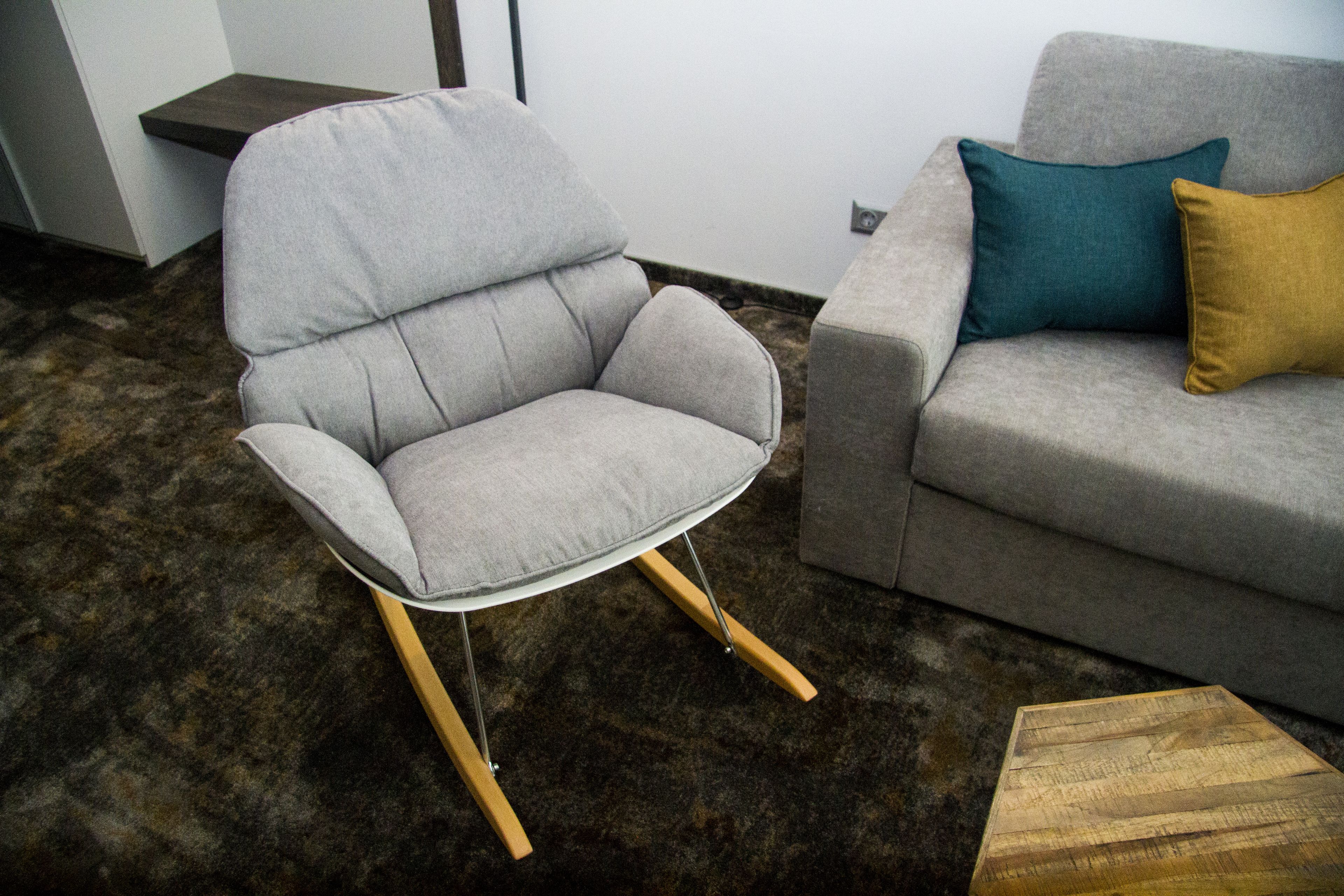 A modern living room with a grey armchair and a grey sofa with a teal and mustard throw pillows.