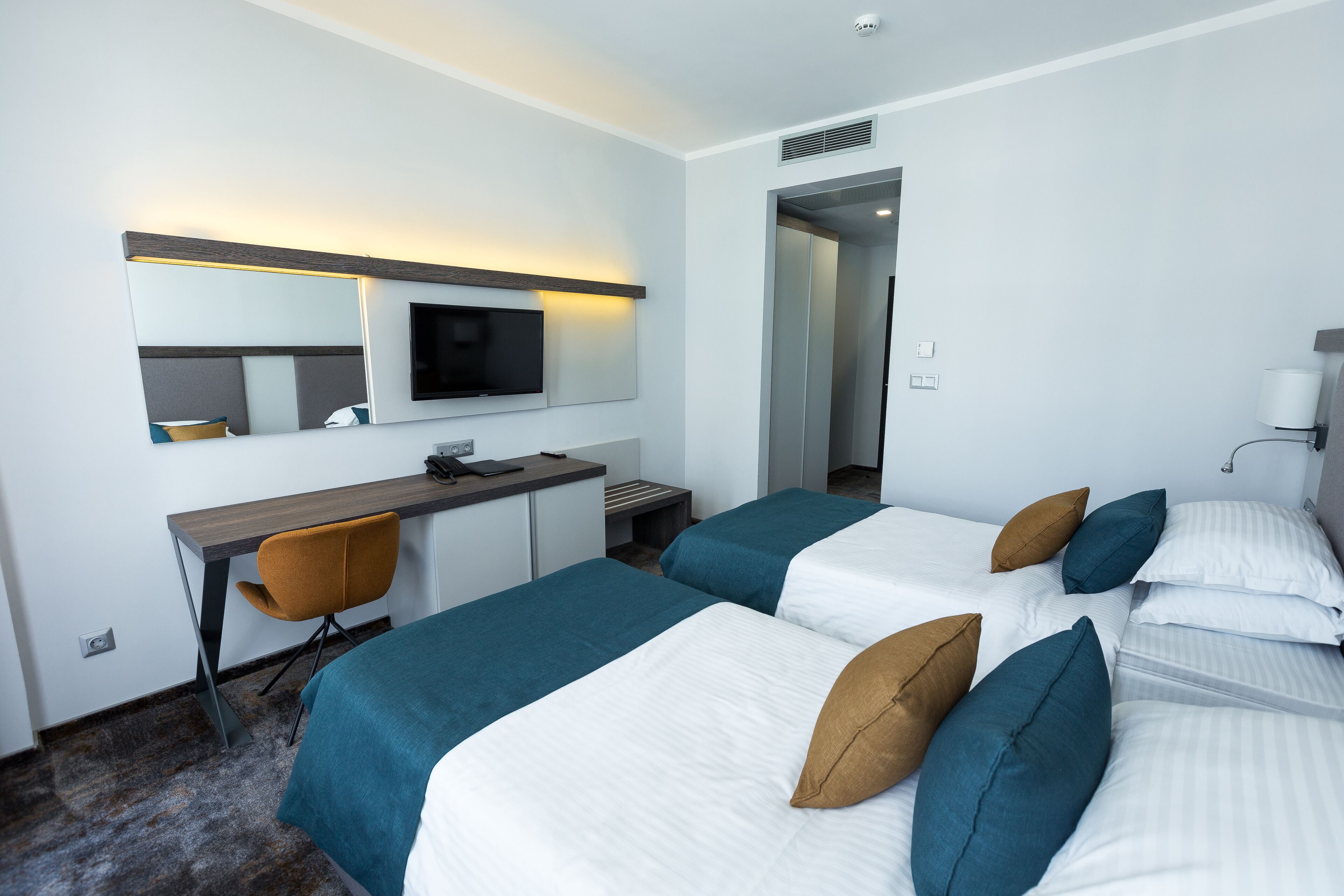 Une chambre d’hôtel avec deux lits, un bureau, une chaise, une télévision et un miroir.