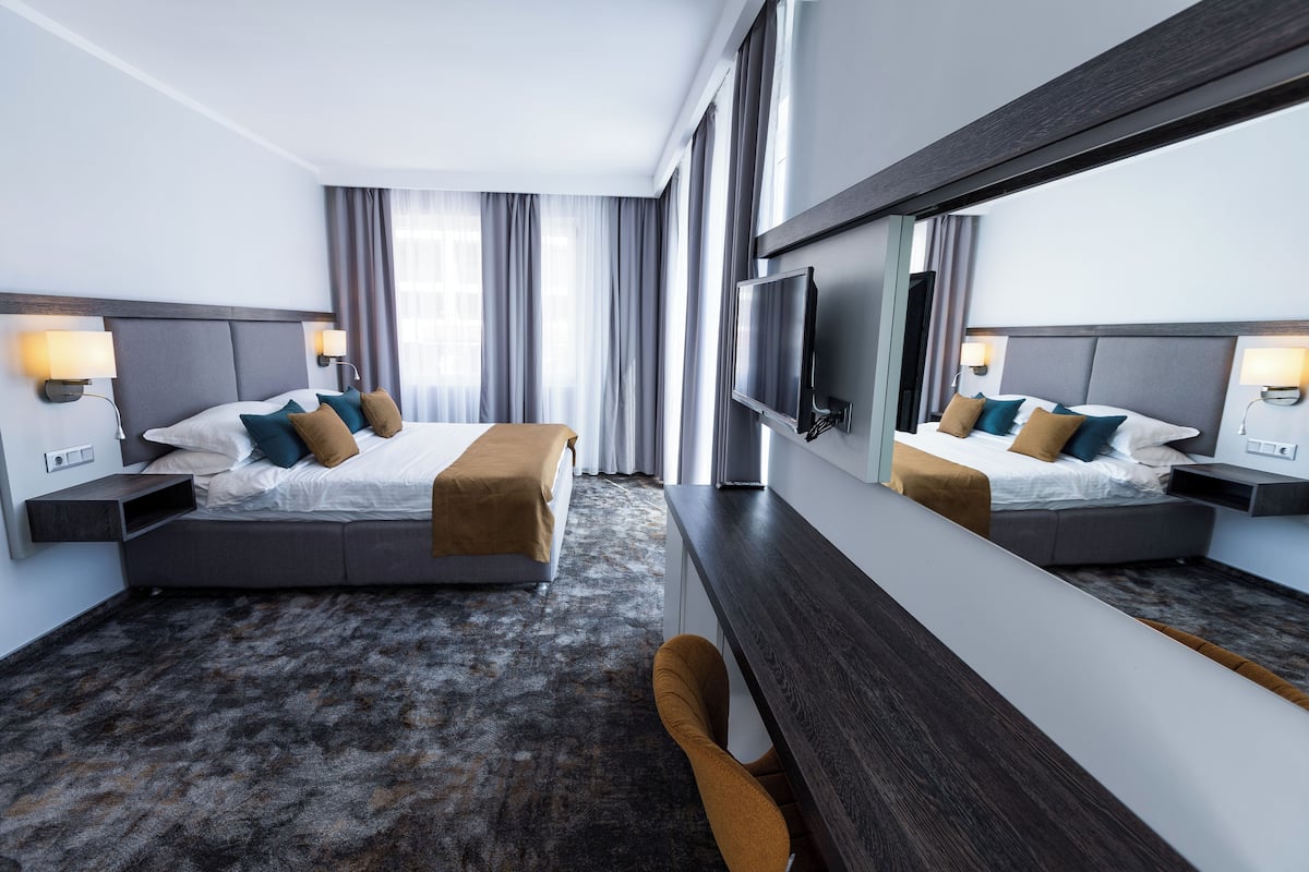 A hotel room with two beds, a large mirror, a TV, and a sofa.