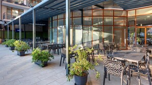 An outdoor dining area with tables and chairs, potted plants, and a covered seating area with a glass wall. - Best Western Plus Premium Inn (Sunny Beach)
