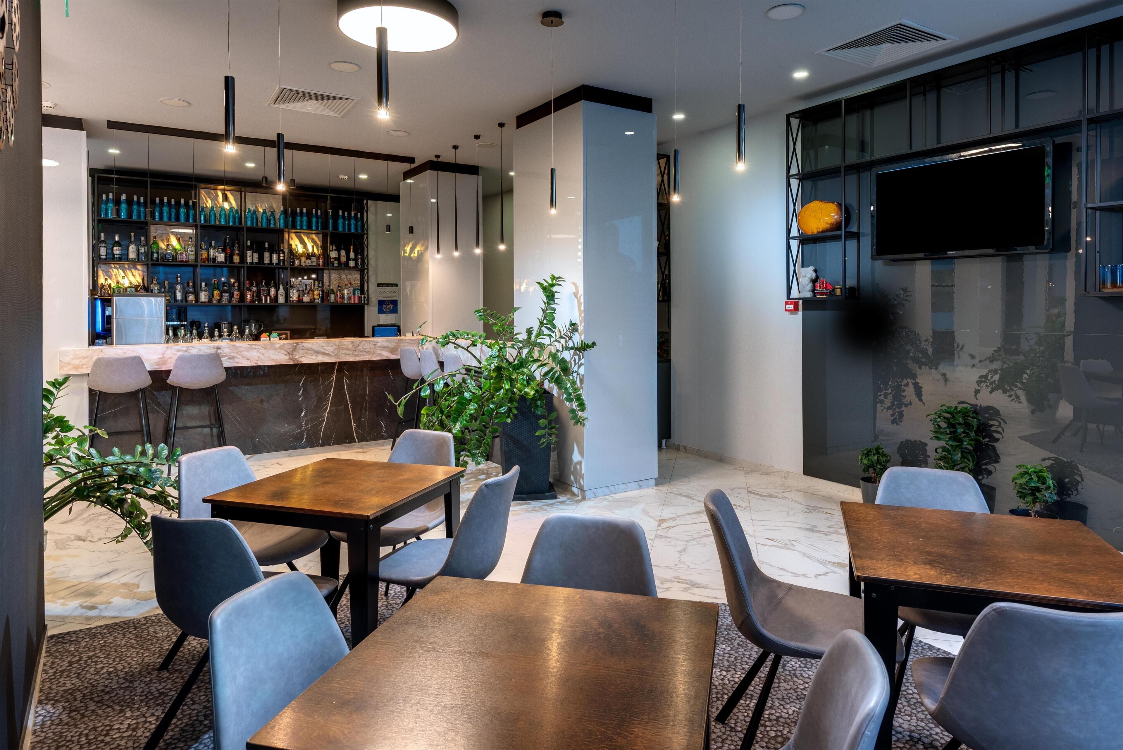 A bar area with shelves of bottles, a TV mounted on the wall, and seating with tables and chairs.