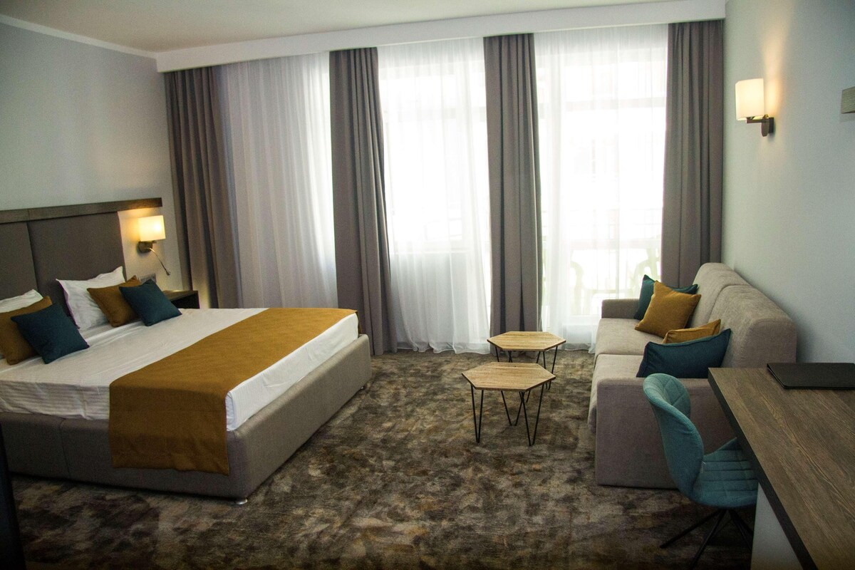 A hotel room with a bed, a sofa, a small table, and a desk.