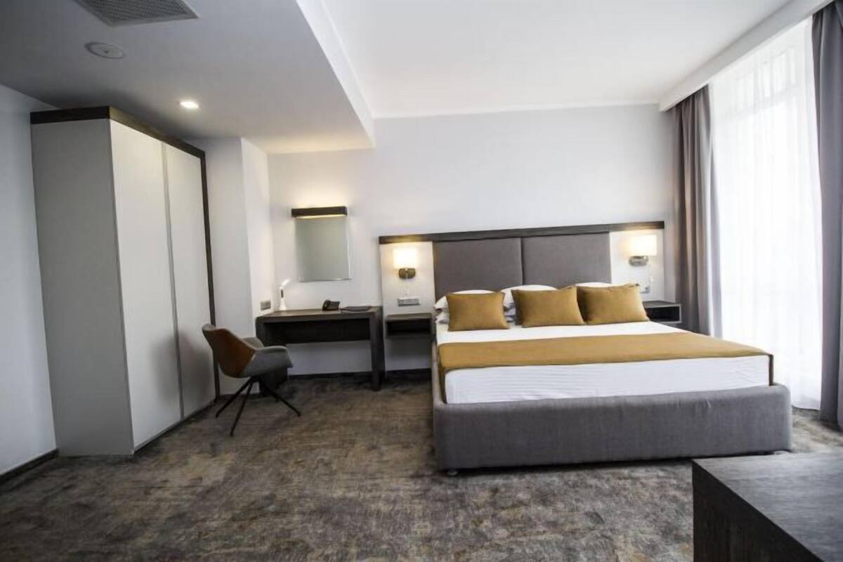 A hotel room with a bed, desk, chair, and a large window.