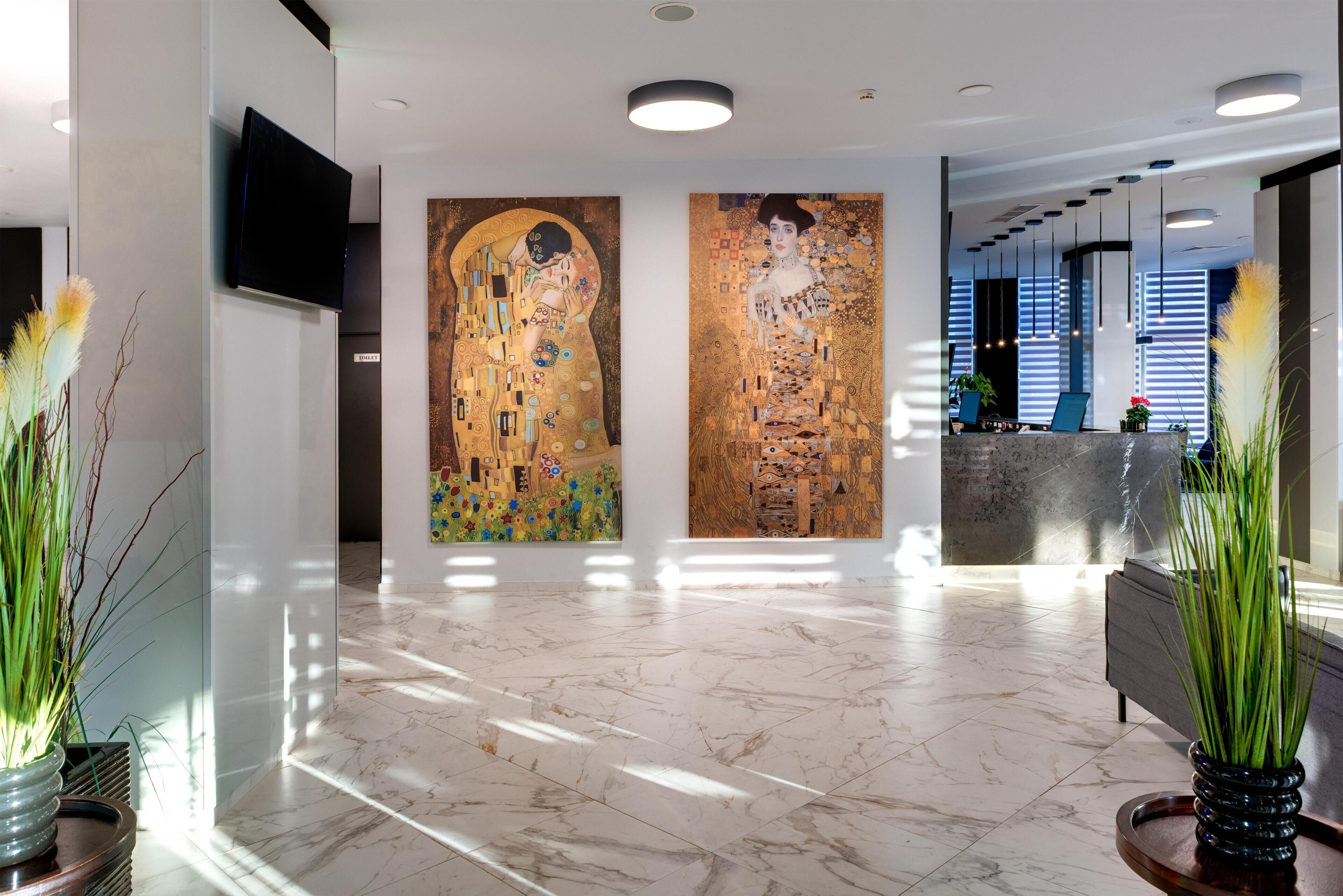 A lobby with a marble floor, two large paintings, a reception desk, and potted plants.