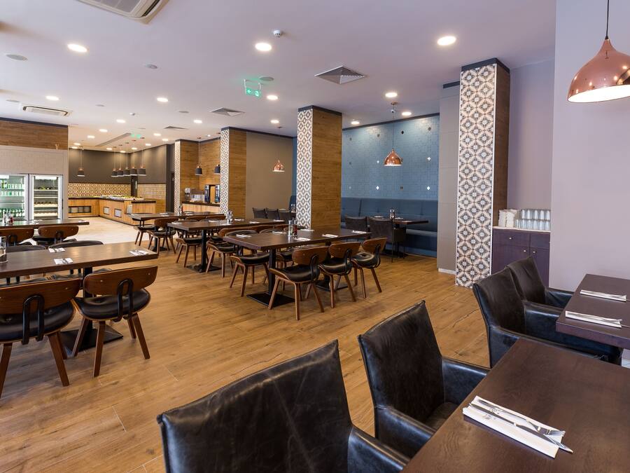 Un restaurante moderno con suelo de madera, varias mesas y sillas, iluminación colgante y una pared con diseño.
