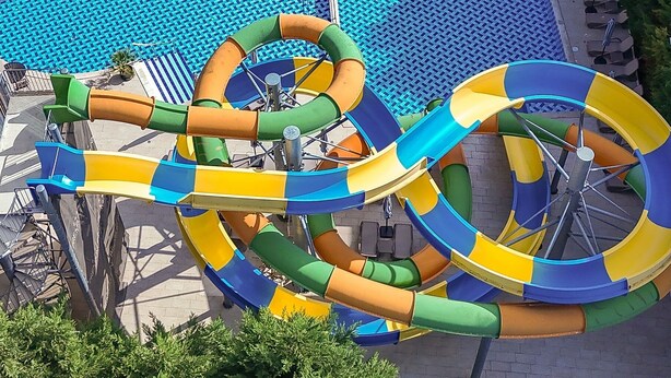 A water slide with multiple loops and curves, surrounded by a pool area with lounge chairs and a tiled deck. - Best Western Plus Premium Inn (Sunny Beach)