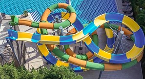 A water slide with multiple loops and curves, surrounded by a pool area with lounge chairs and a tiled deck.