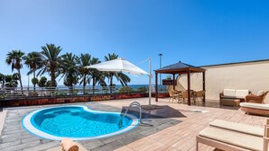 Un área de piscina en la azotea con sillones, un espacio de descanso cubierto y vista al océano.