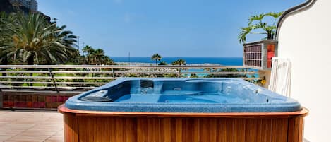 A wooden hot tub with a view of the sea and palm trees.