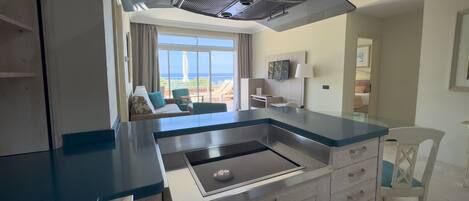 A modern kitchen with a built-in stove, a dining area with a table and chairs, and a view of the ocean through large windows.