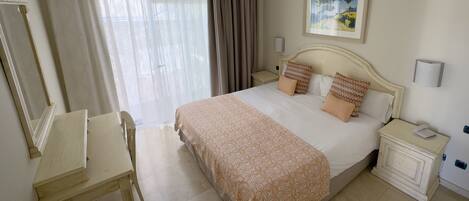 A hotel room with a bed, bedside tables, a desk, a chair, and a painting on the wall.