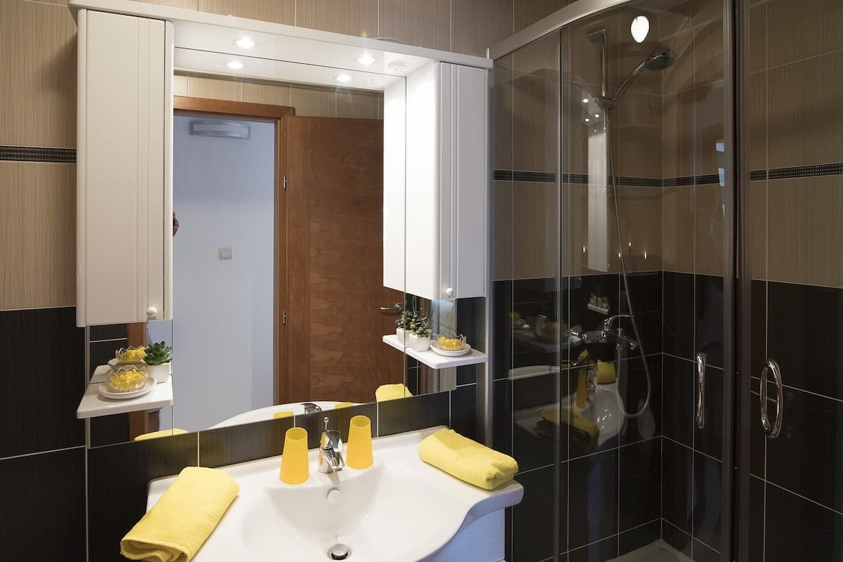 A modern bathroom with a large mirror, a sink with yellow towels, and a glass-enclosed shower area.