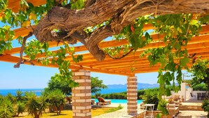 A covered outdoor area with a pool, seating, and a view of the sea. - Paros Afrodite Luxury Villas (Paros)