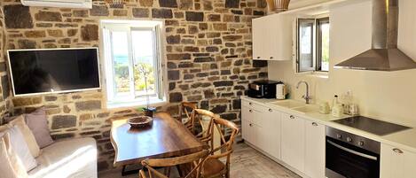 A cozy kitchen with a stone wall, wooden dining table, and white cabinets.