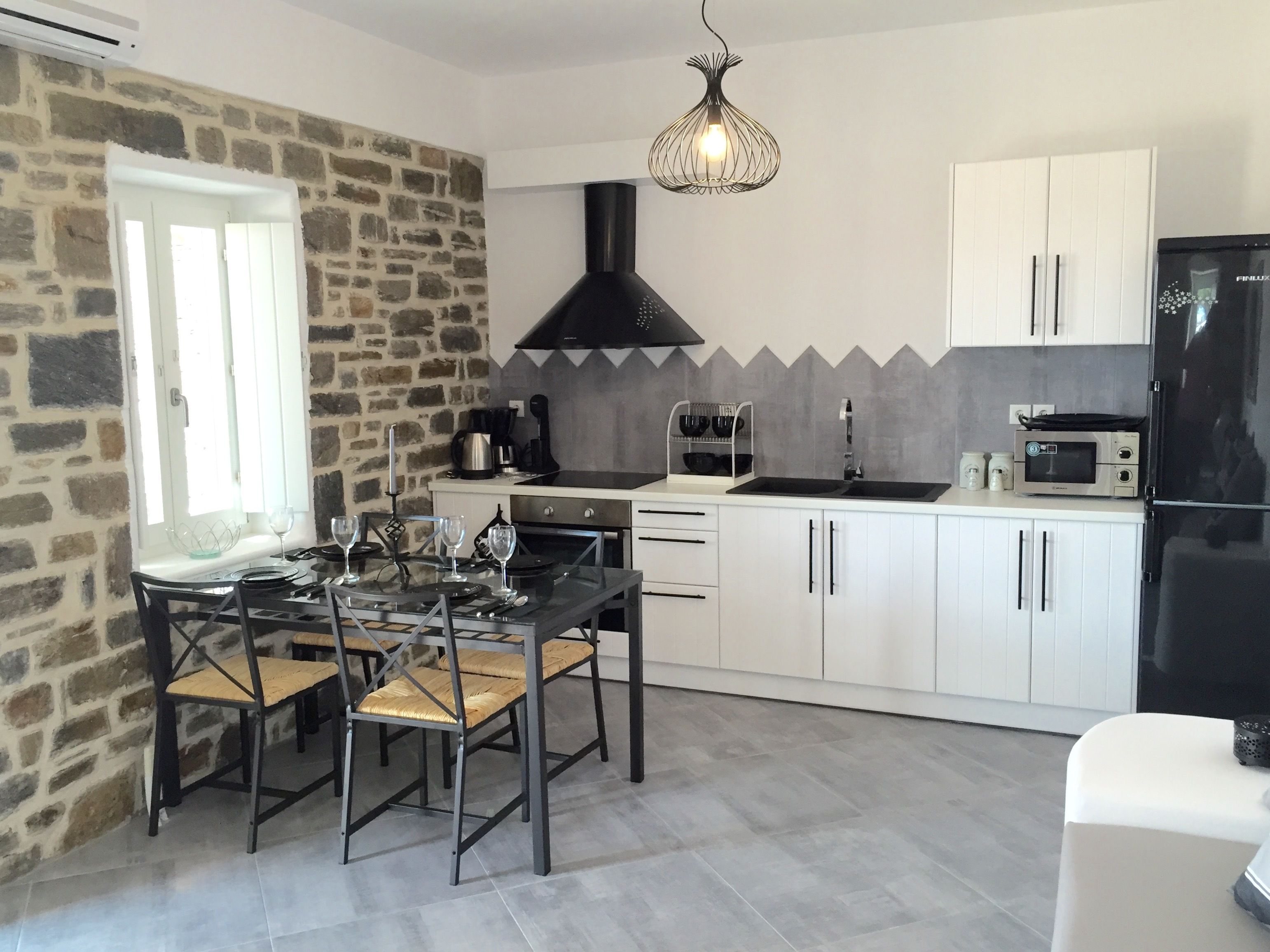 Una cocina moderna con armarios blancos, una estufa negra y un microondas. Hay una mesa de comedor con sillas y una lámpara colgante.