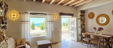 Una habitació acollidora amb una paret de pedra, un sostre de fusta, zona de menjador amb taula i cadires, i vistes a l'exterior.