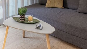 A modern living room with a grey sofa, a small round table with a plant and candle, and a framed artwork on the wall. - Elvita Apartments (Athens)
