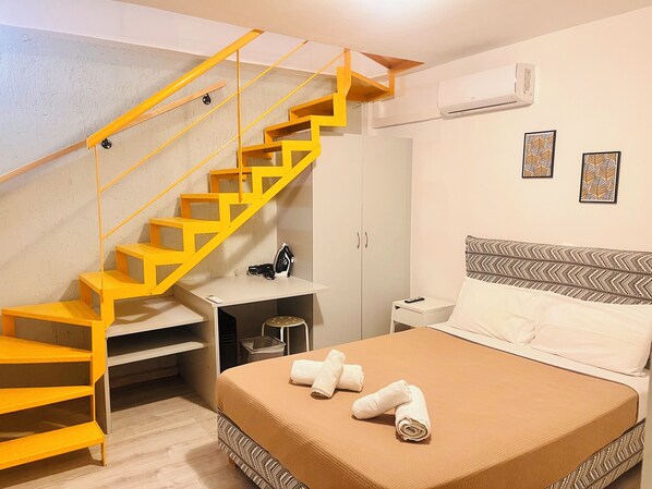 A bedroom with a bed, a nightstand, a desk, a chair, a wardrobe, and a staircase.