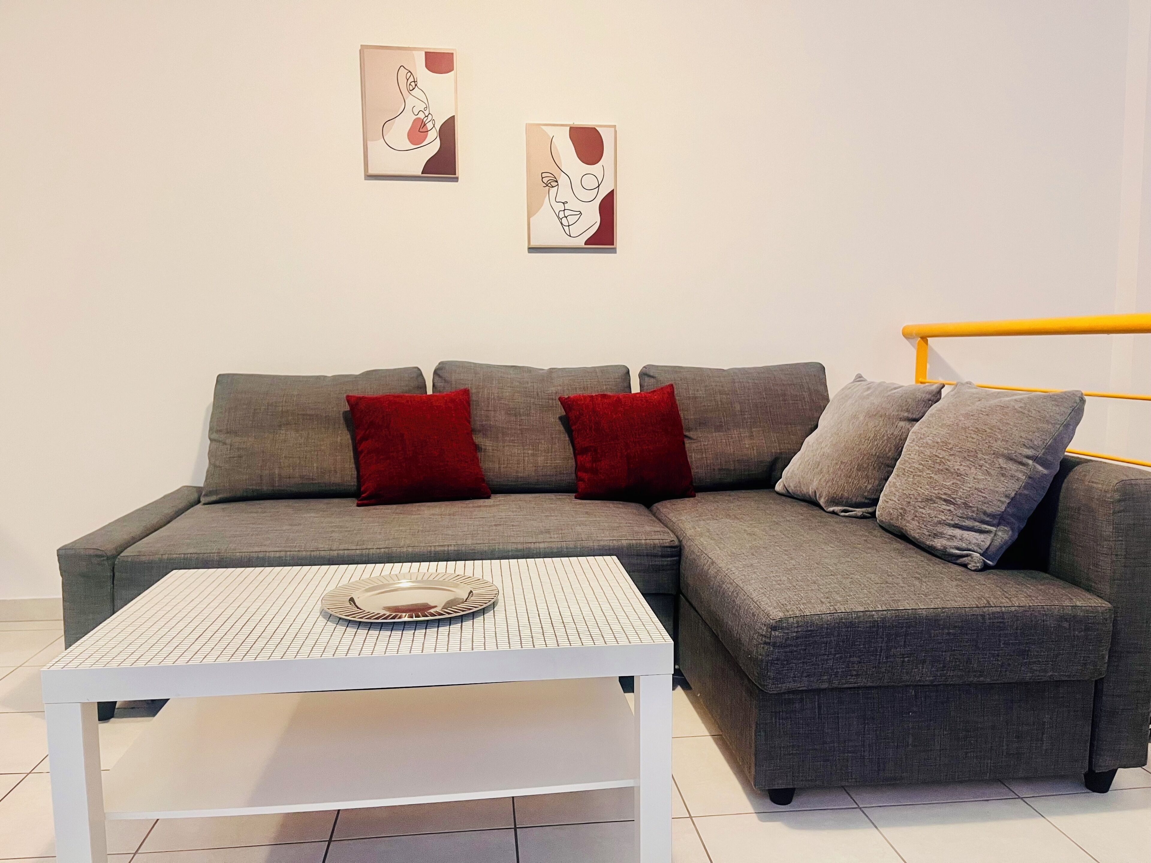 A modern living room with a grey sectional sofa, red and grey cushions, a white coffee table, and two abstract paintings on the wall.