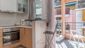 A compact kitchen with modern appliances, a balcony with a view of a colorful building, and a white chair. - Elvita Apartments (Athens)