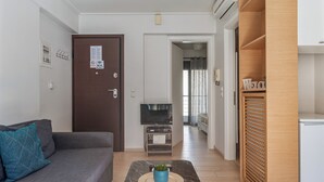 A modern living room with a grey sofa, a TV on a wooden stand, a small table with a plant, and a wooden cabinet. - Elvita Apartments (Athens)