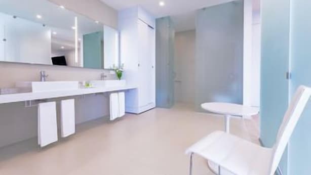Een moderne badkamer met een grote spiegel, een witte wastafel en een witte stoel.
