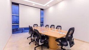 Een vergaderzaal met een lange tafel, zwarte stoelen en een groot scherm.