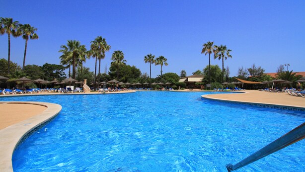 A large pool with clear blue water, surrounded by palm trees and lounge chairs. - Hotel Garbí Cala Millor (Sant Llorenc des Cardassar)