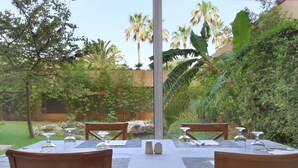 An outdoor dining area with a table set for two, surrounded by lush greenery and palm trees. - Hotel Garbí Cala Millor (Sant Llorenc des Cardassar)