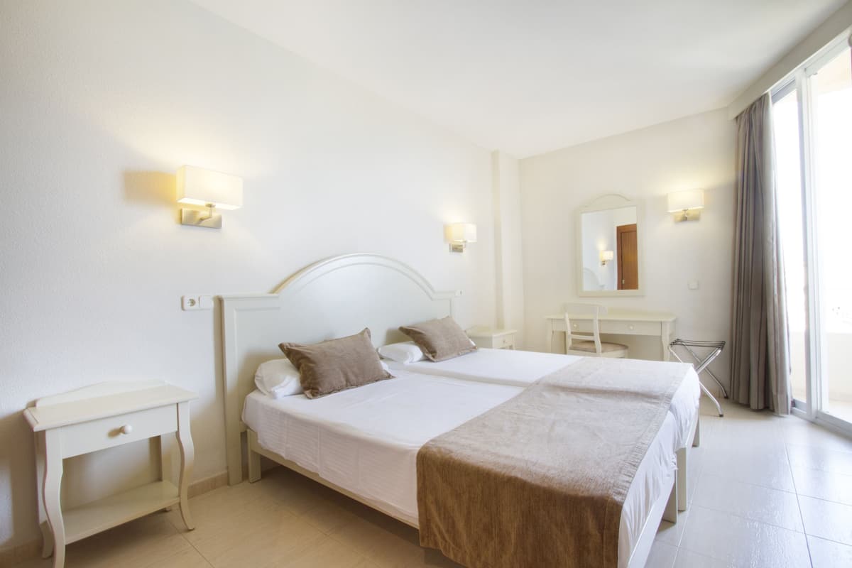 A hotel room with two beds, a desk, a chair, and a mirror.
