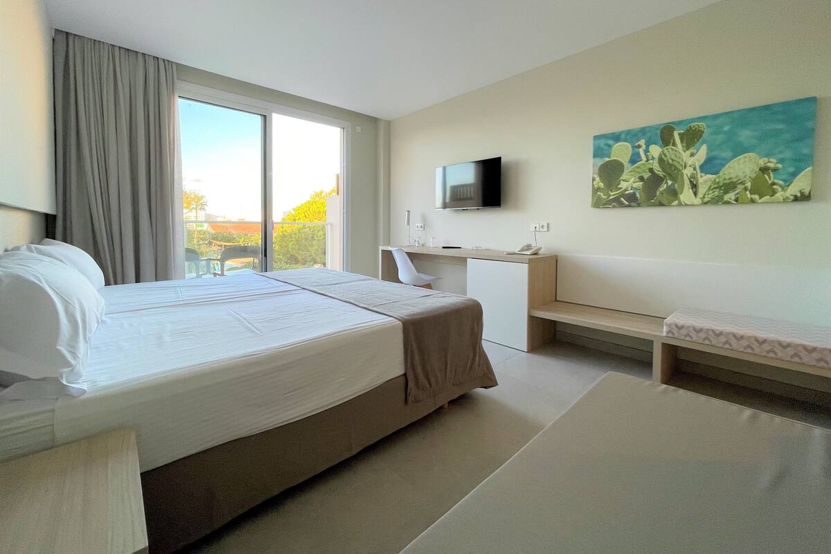 A hotel room with a bed, a desk, a television, and a painting.