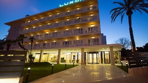 A multi-story hotel with balconies, a well-lit entrance, and palm trees. - Hotel Luxor (Palma de Mallorca)