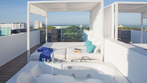 A rooftop terrace with a white bathtub, a sofa with a blue towel, and a view of the sea and buildings. - Hotel Luxor (Palma de Mallorca)