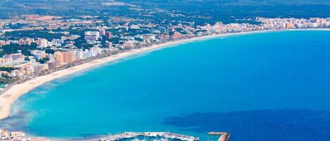 Vista aérea de una ciudad costera con una extensa playa de arena, un puerto deportivo con numerosos barcos y densa edificación urbana.