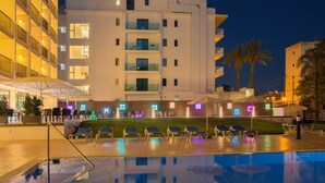 A poolside area with lounge chairs and umbrellas, a reflection pool, and a building with balconies and windows. - Hotel Luxor (Palma de Mallorca)