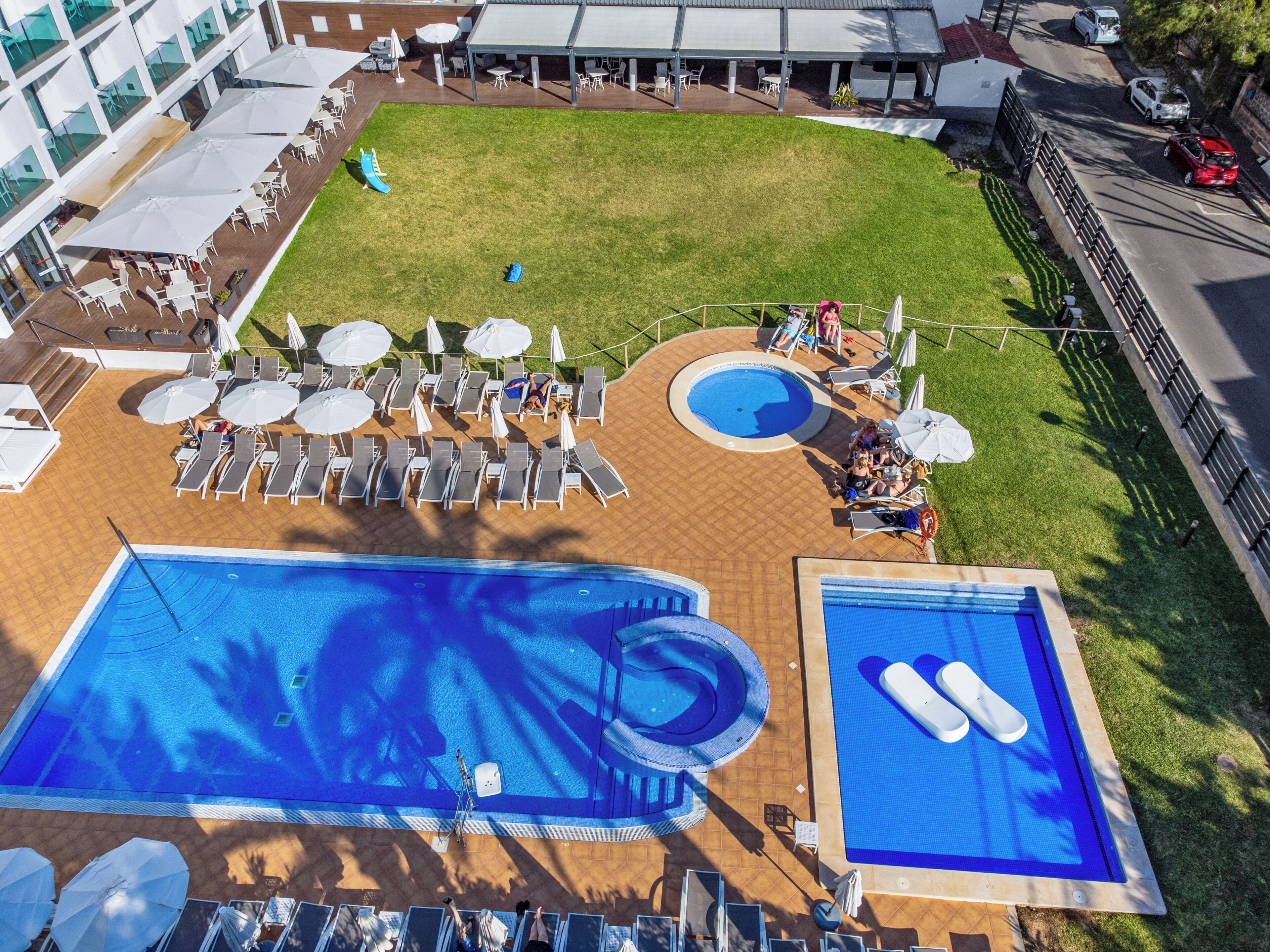 A rooftop pool area with multiple swimming pools, sun loungers, and umbrellas.