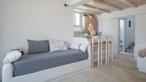 A modern living room with a sofa, a dining area with chairs, and a kitchen in the background. - Depis Bay Apartments (Naxos)