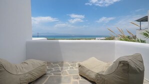 A balcony with a stone floor and two beige cushions, overlooking a coastal view with a clear sky. - Depis Bay Apartments (Naxos)