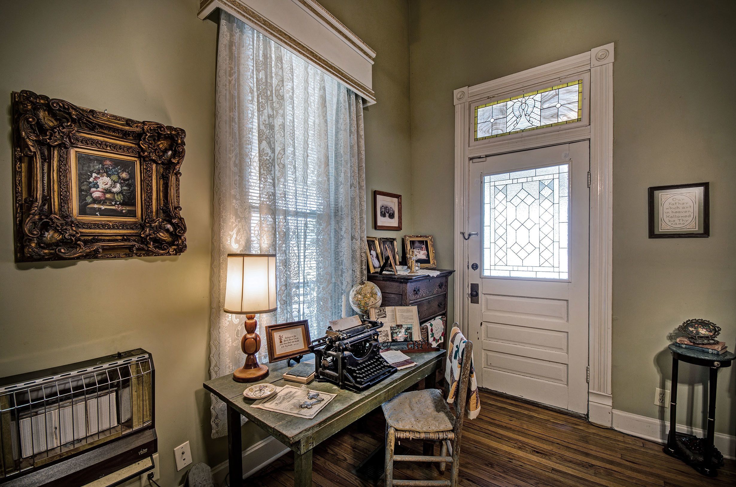 A room with a vintage typewriter, a radiator, a wooden floor, and a door with stained glass.