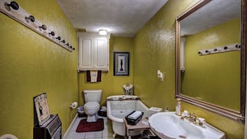 A bathroom with a white bathtub, a white sink, and a toilet. There is a mirror on the wall and a shelf with various items.