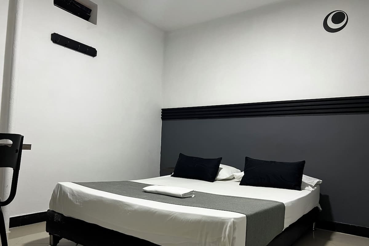 A neatly made bed with a white and gray bedspread, two black pillows, and a small white pillow.