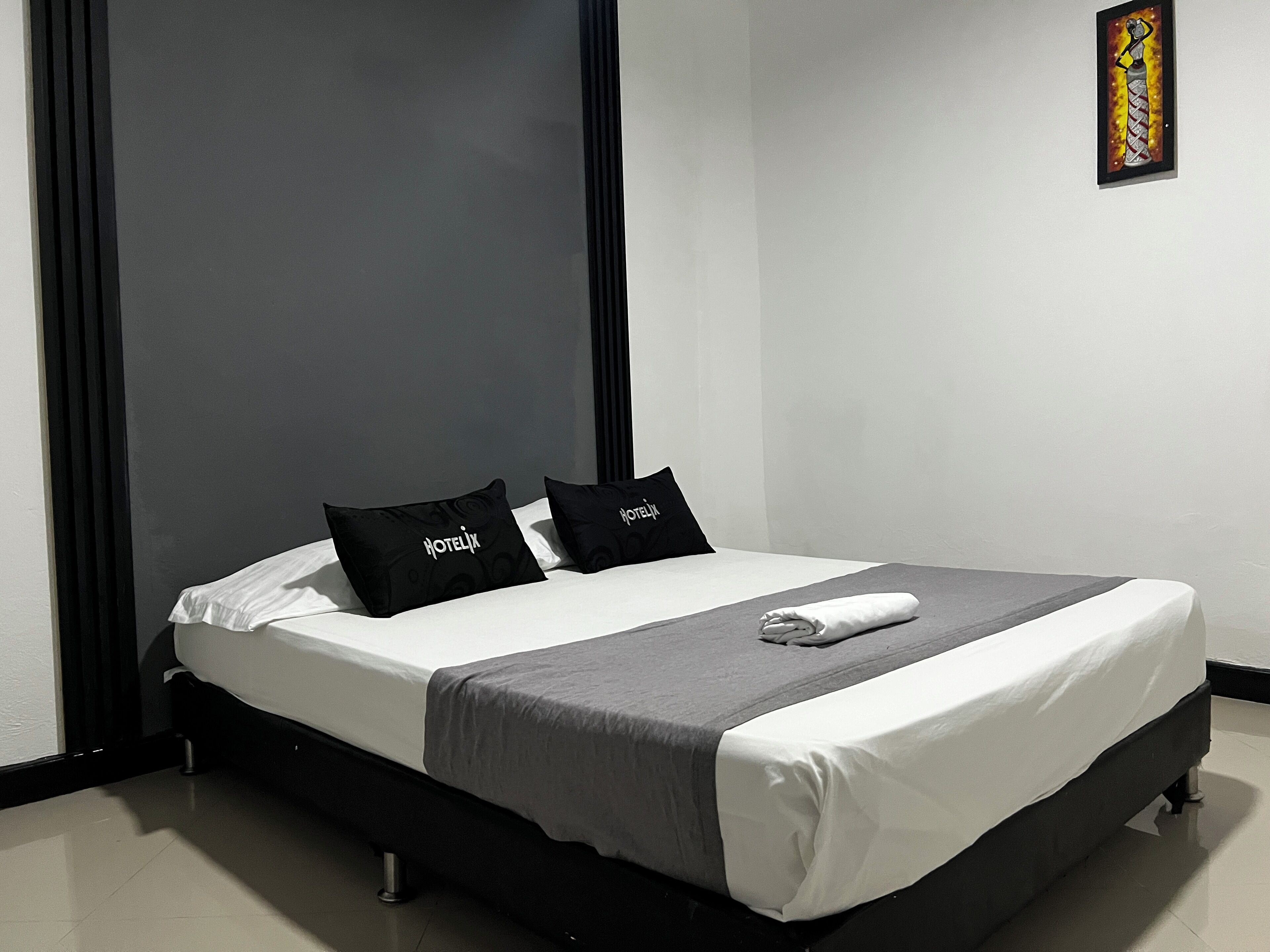 Un lit bien fait, avec une literie noire et blanche, deux oreillers sur lesquels est inscrit le mot «HÔTEL», et une serviette pliée posée sur le lit.
