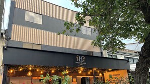 A modern building with a black awning, outdoor seating area with string lights, and potted plants. - Hotel Laureles de Aburra Medellin (Medellín)