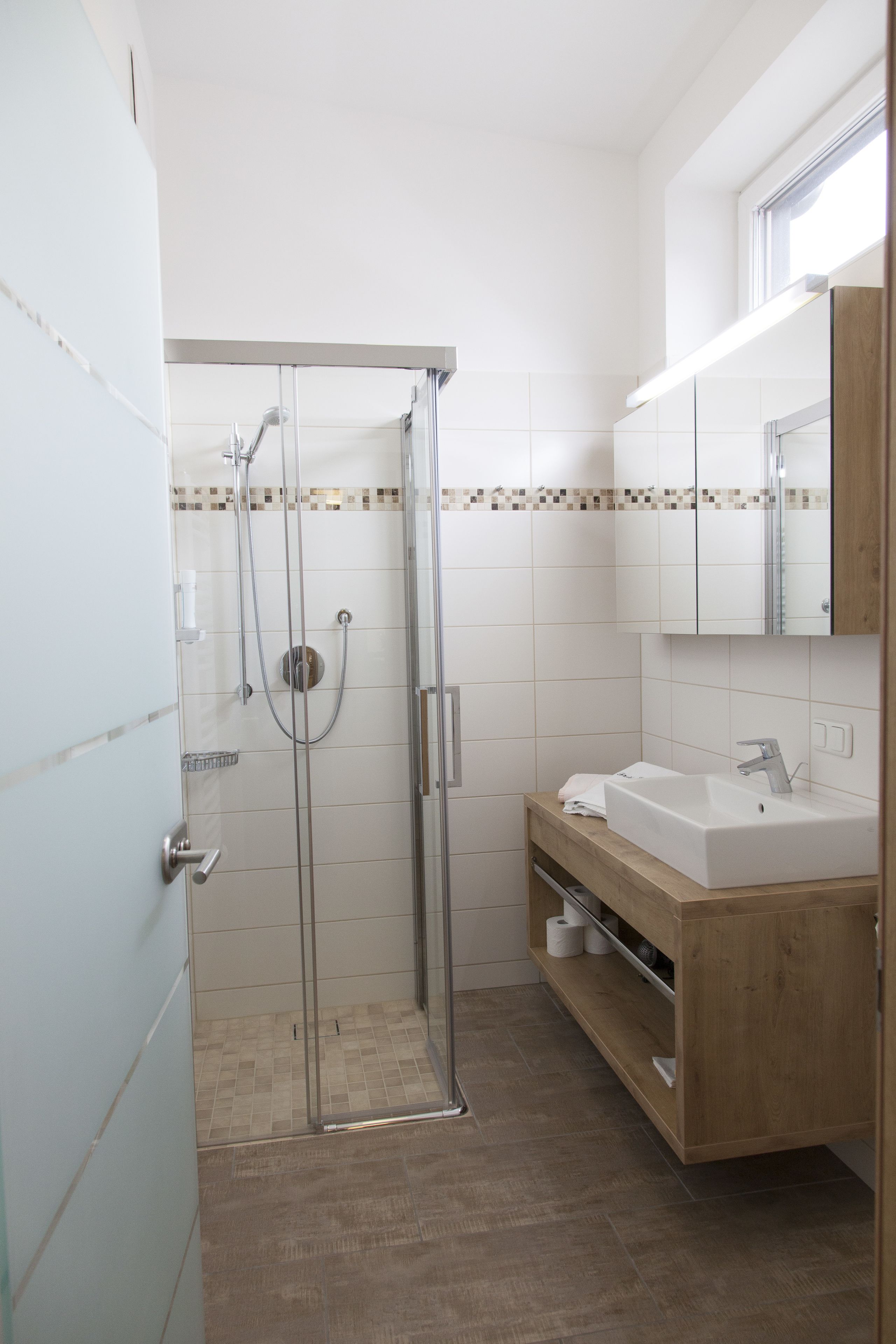A bathroom with a glass shower enclosure, a wooden vanity with a sink, and a mirror above the vanity.