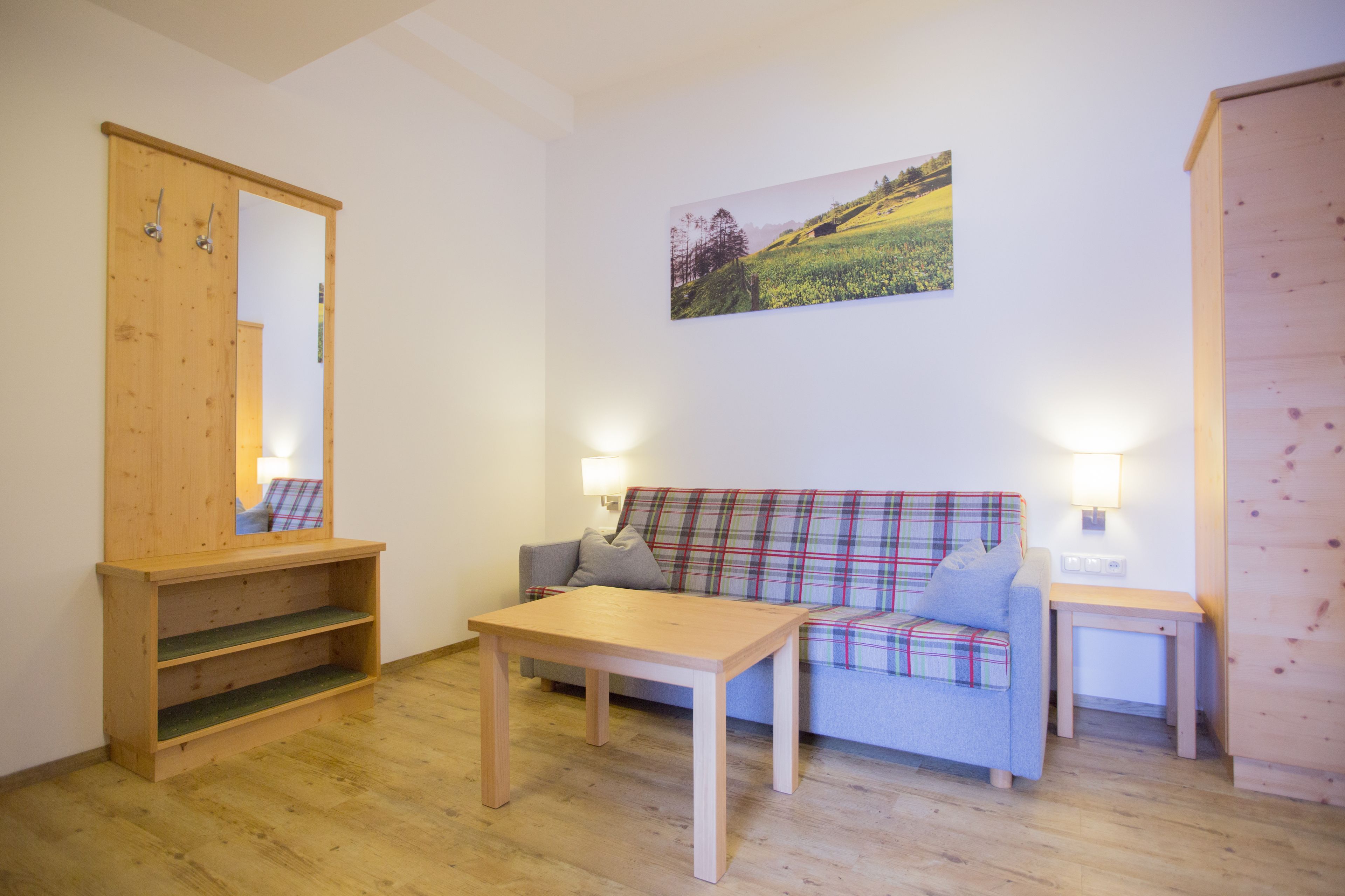 Ein gemütliches Zimmer mit Holzboden, einem karierten Sofa, einem Holztisch, einem Spiegel und einem an der Wand hängenden Bild.