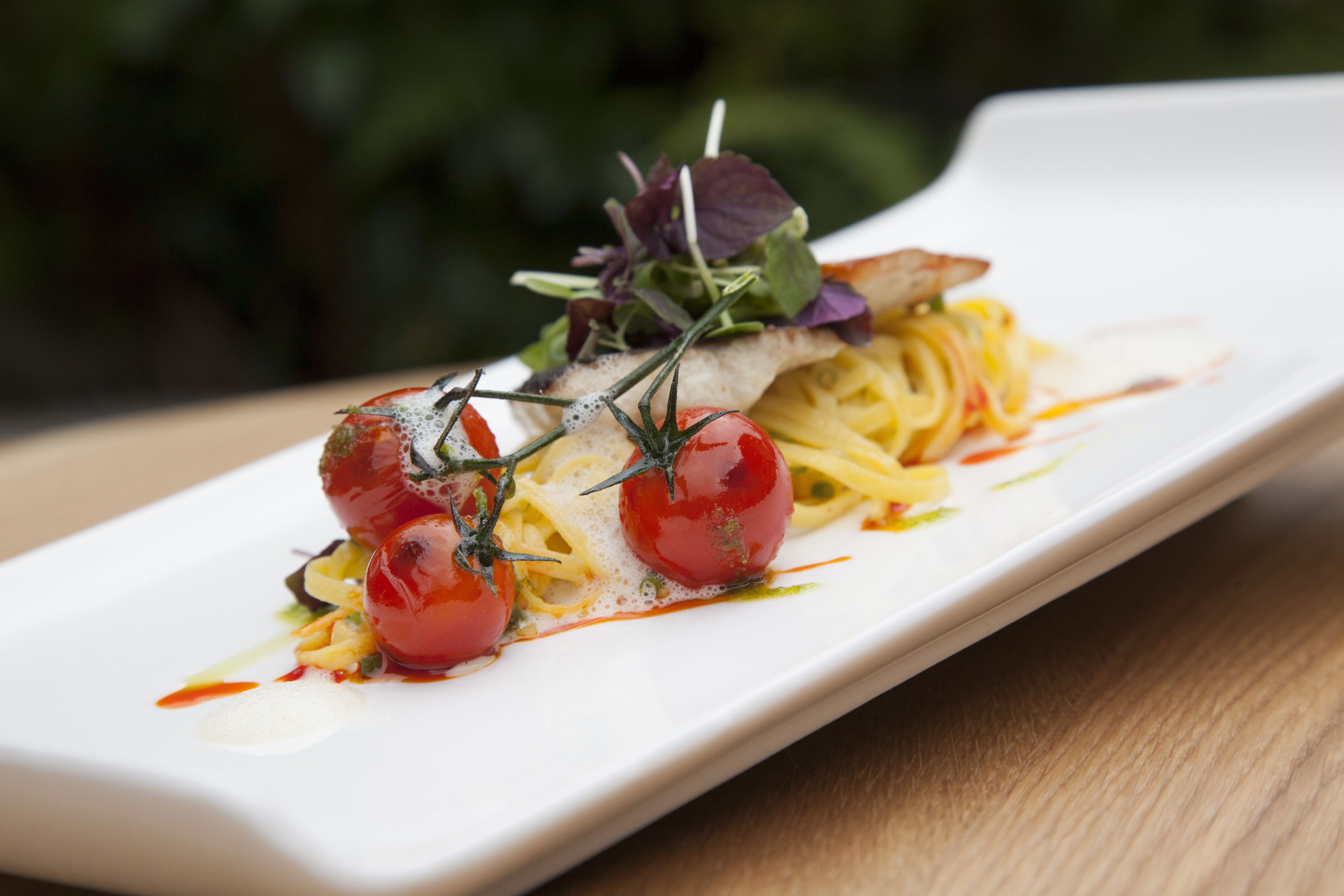 A white rectangular plate with a pasta dish, cherry tomatoes, and greens.