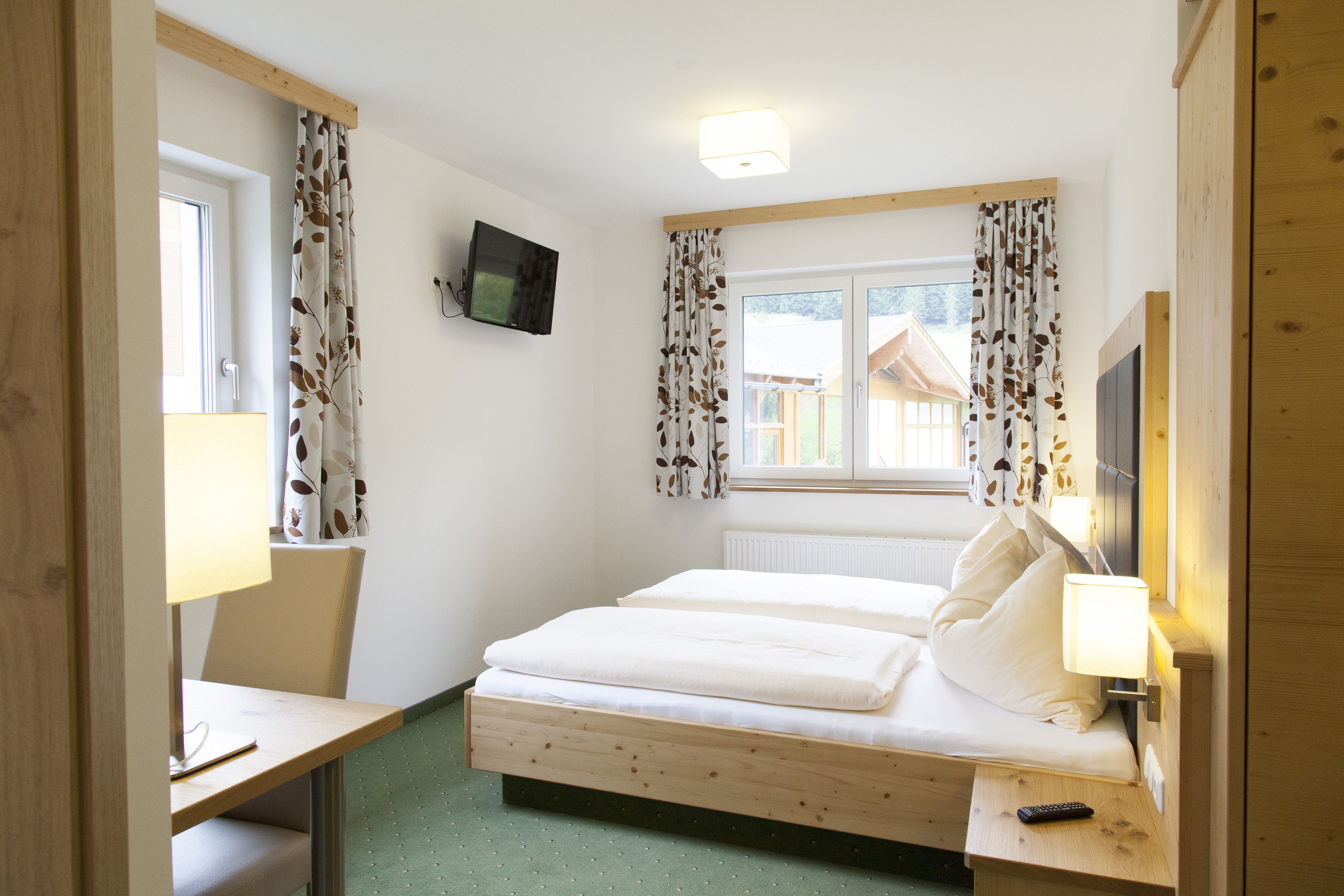Une chambre à coucher avec un lit, un bureau, une chaise, un téléviseur et une fenêtre avec des rideaux.