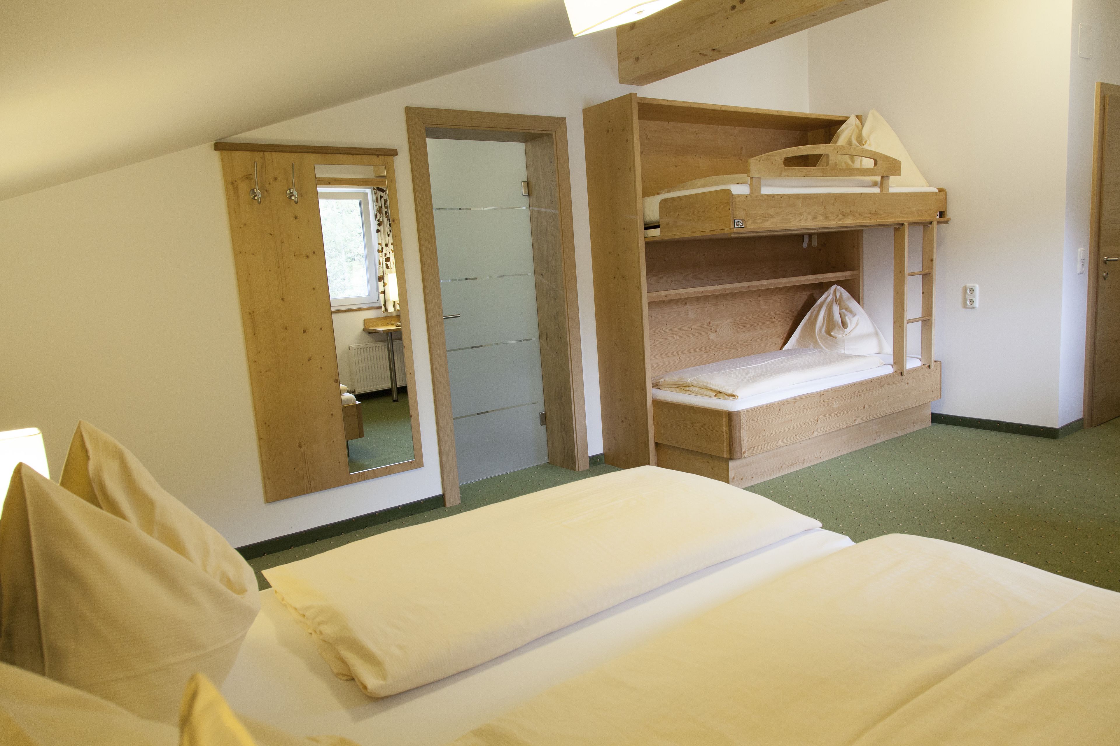 A room with bunk beds, a mirror, and a door leading to another room.