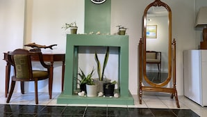 Um quarto com lareira verde, uma cadeira de madeira, um espelho e um relógio na parede.